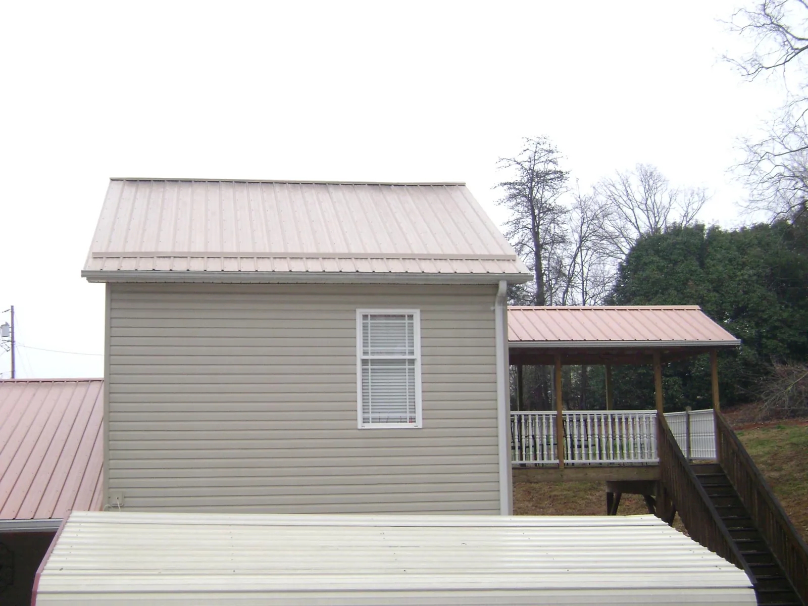 Tan metal roofs on a two story addition and attached porch, from a Roof Replacement job in Hilo
